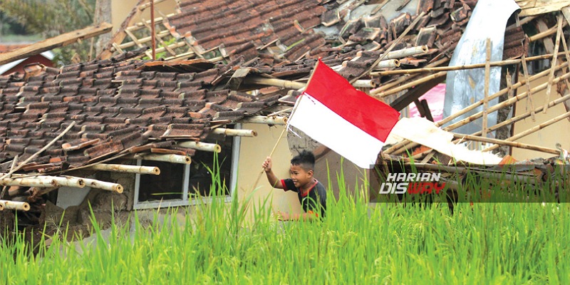 Seorang anak membawa bendera merah putih diantara reruntuhan akibat gempa Cianjur/Disway